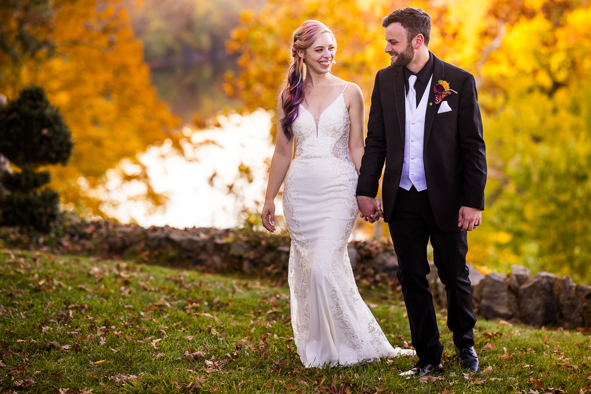 Murray Hill Wedding Photographer, lisa rhinehart, captures this candid portrait of the bride and groom as they walk amongst the vibrant fall foliage of leesburg virginia beside the Potomac river 