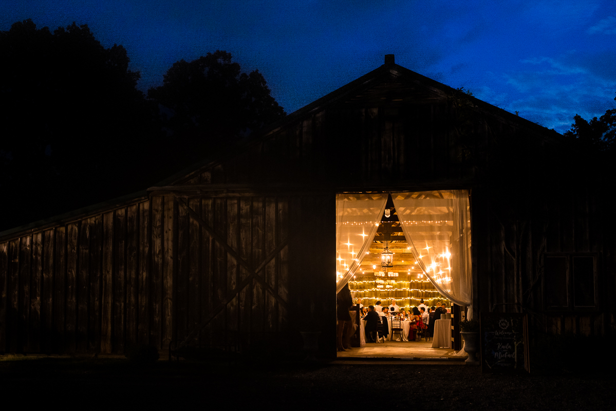 Murray Hill Wedding Photographer, lisa rhinehart, captures this night shot from outside of the barn looking in featuring a vibrant blue sky and a warm yellow barn 