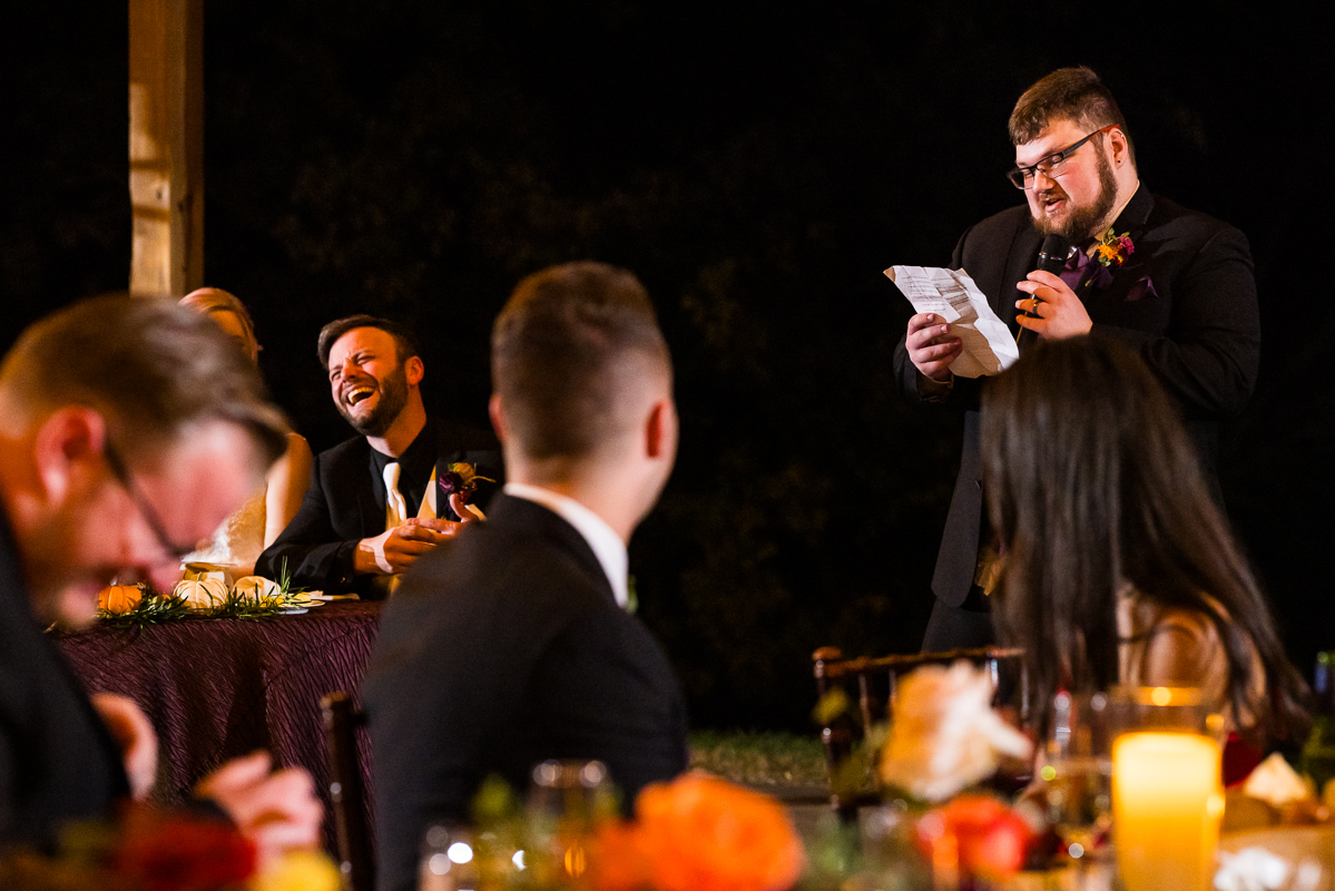 candid wedding photographer, lisa rhinehart captures this authentic moment of the wedding party giving speeches while the groom laughs during this barn wedding reception in Leesburg va