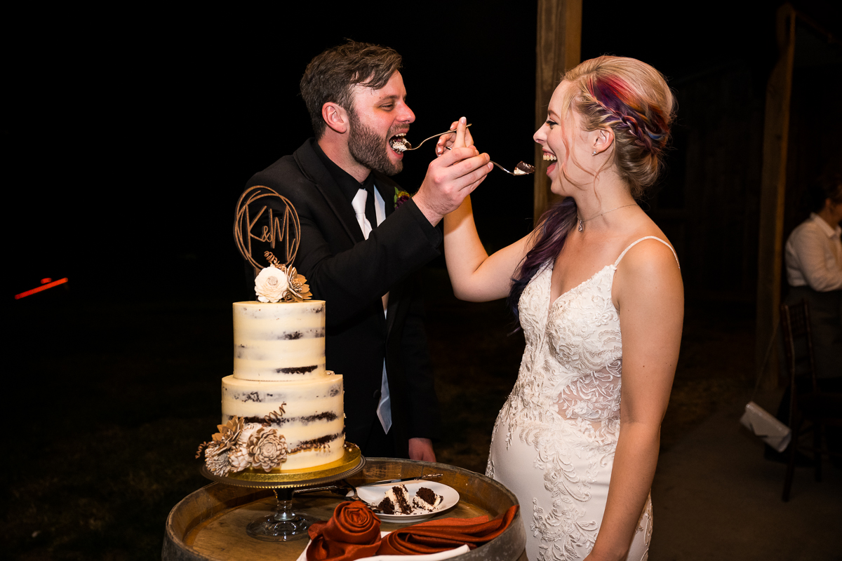 candid image of the bride and groom as they share cake with each other during their barn wedding reception at Murray hill in Virginia a wedding venue located in Leesburg va beside the Potomac river
