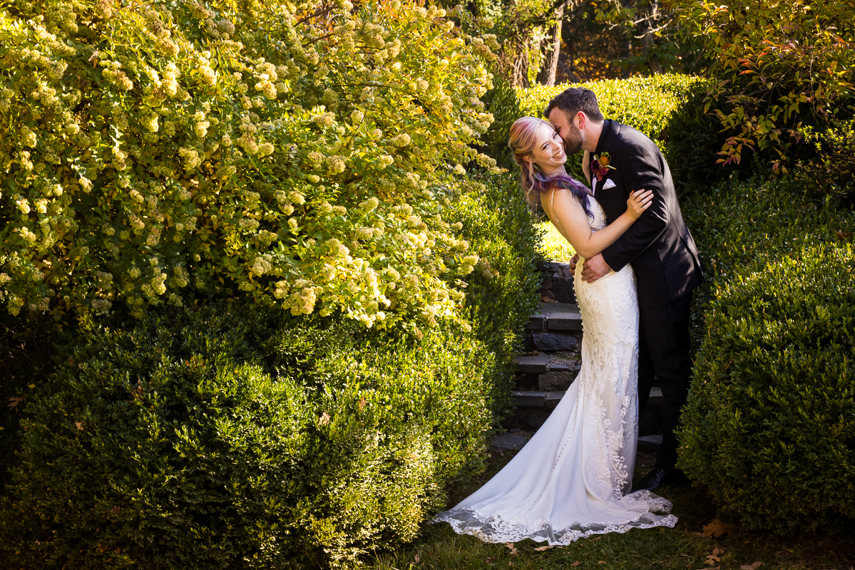 Murray hill wedding photographer, lisa rhinehart, captures this image of the bride and groom as they hug and kiss one another in this little outdoor walkway surrounded by the fall foliage of leesburg va