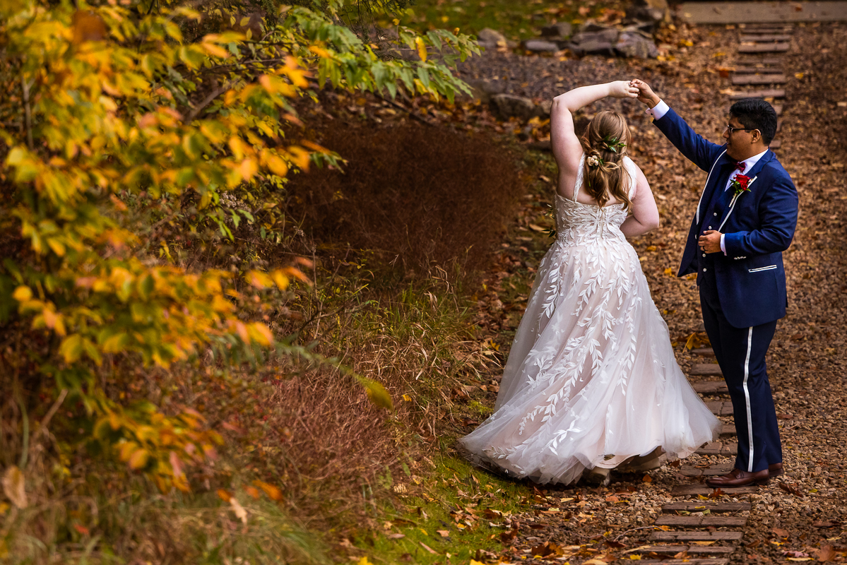 bedford pa wedding photographer, lisa rhinehart, captures this outdoor portrait of the bride and the groom as the groom spins the bride while surrounded by the vibrant, colorful fall foliage