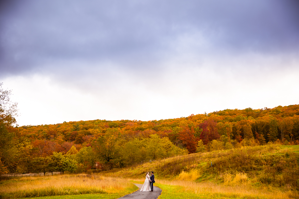 creative Omni wedding photographer, lisa rhinehart, captures this vibrant, colorful landscape image of the bride and groom during their romantic portraits as they walk into the colorful, vibrant fall foliage at the omni bedford springs in Bedford, pa 