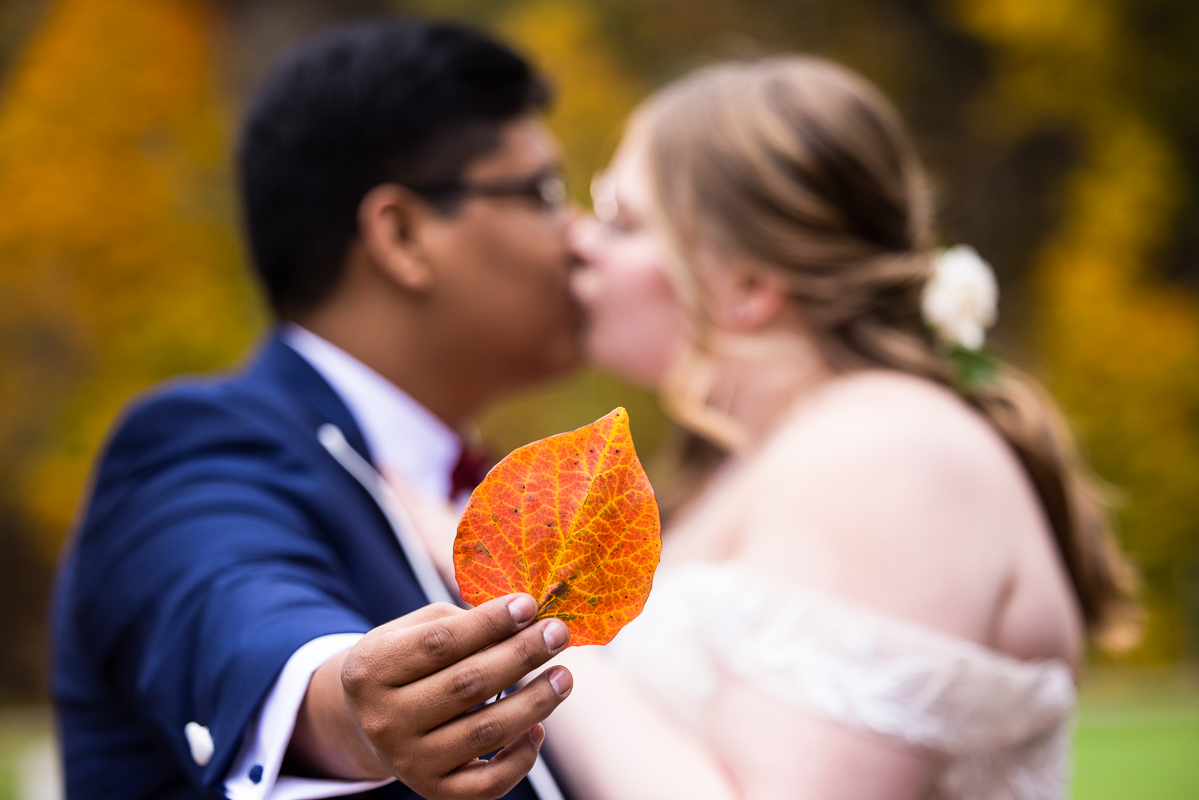 creative Omni wedding photographer, lisa rhinehart, captures this creative, unique image of the bride and groom out of focus as they kiss behind the in focus, vibrant orange leaf outside of the omni bedford springs