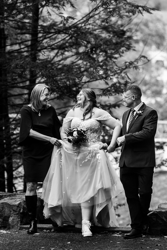 candid black and white image of the bride as she walks arm in arm with her mom and dad down the aisle to her outdoor wedding ceremony at the omni in Bedford springs pa 
