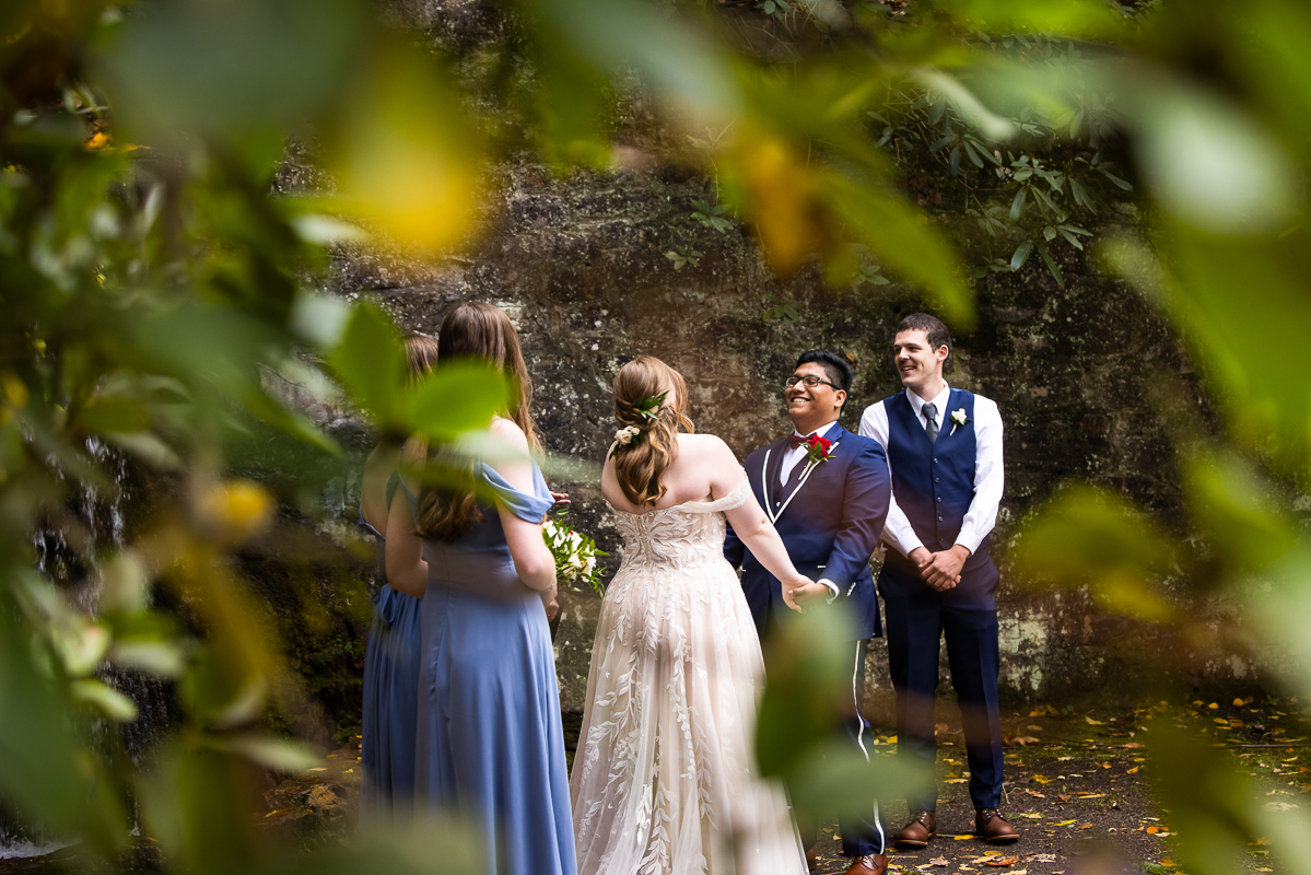 creative Omni wedding photographer, lisa rhinehart, captures this unique, creative image peeking through the fall foliage of the bride and groom as they laugh and smile with each other during their outdoor fall wedding ceremony in Bedford pa 