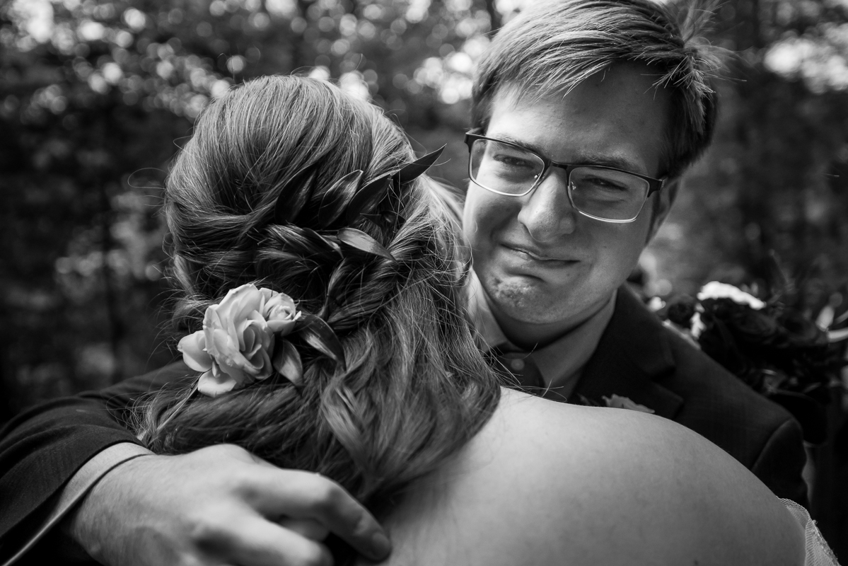 emotional, candid black and white image of the bride as she hugs her brother at the end of this outdoor wedding ceremony captured by best pa wedding photographer, lisa rhinehart