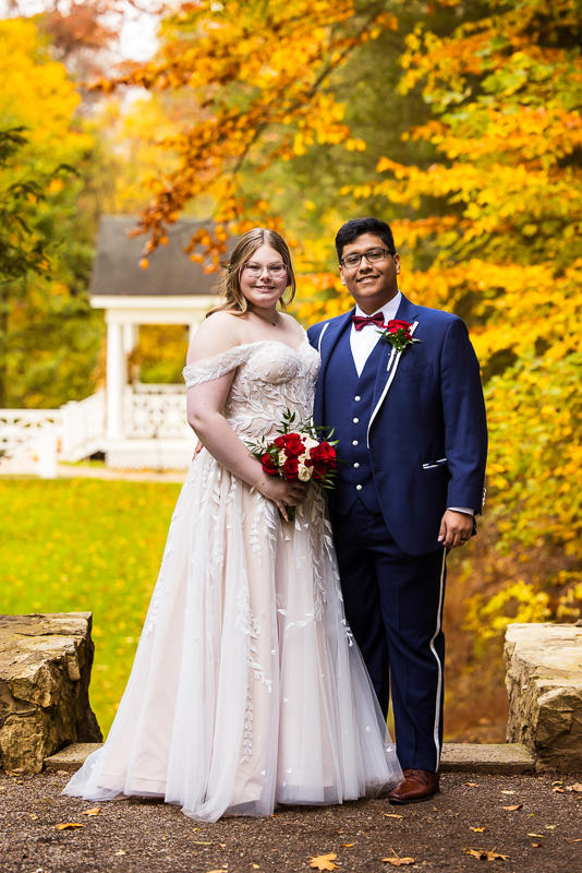 pa wedding photographer, lisa rhinehart, captures this traditional portrait of the bride and groom smiling at the camera surrounded by the vibrant, colorful fall foliage at omni bedford springs, pa 
