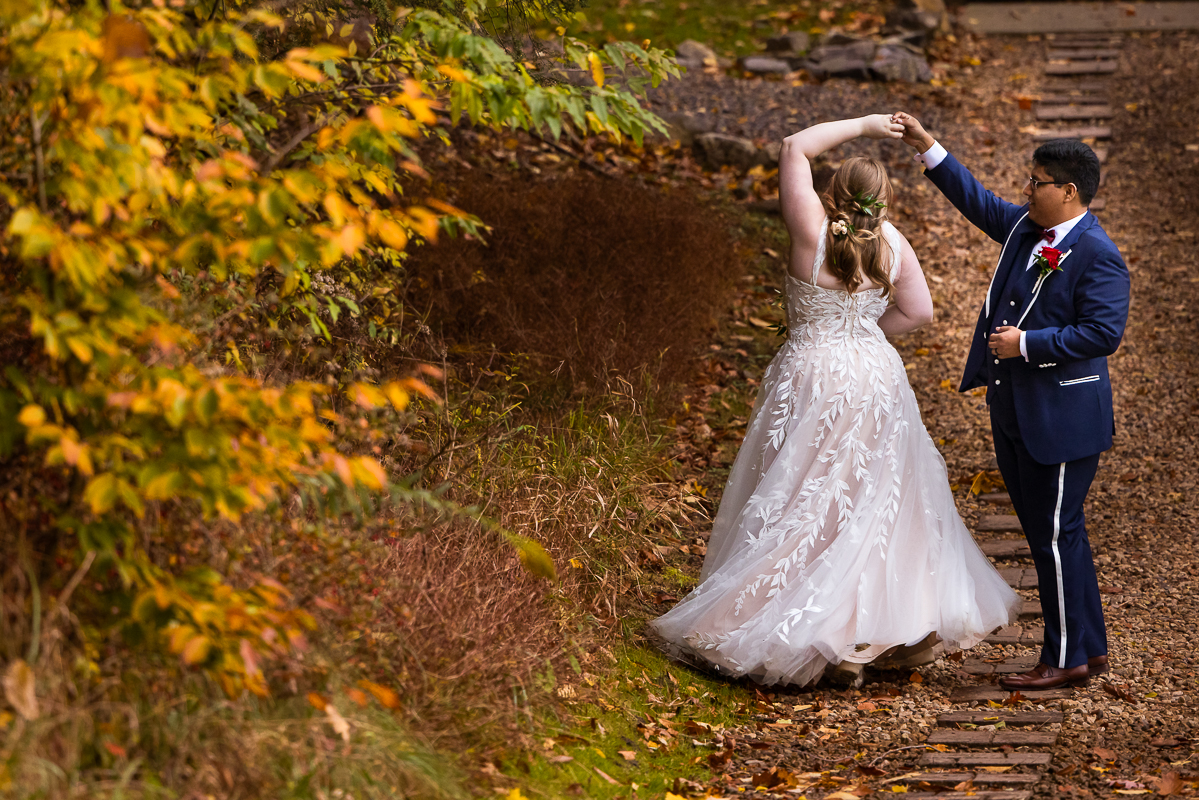 bedford pa wedding photographer, lisa rhinehart, captures this outdoor portrait of the bride and the groom as the groom spins the bride while surrounded by the vibrant, colorful fall foliage