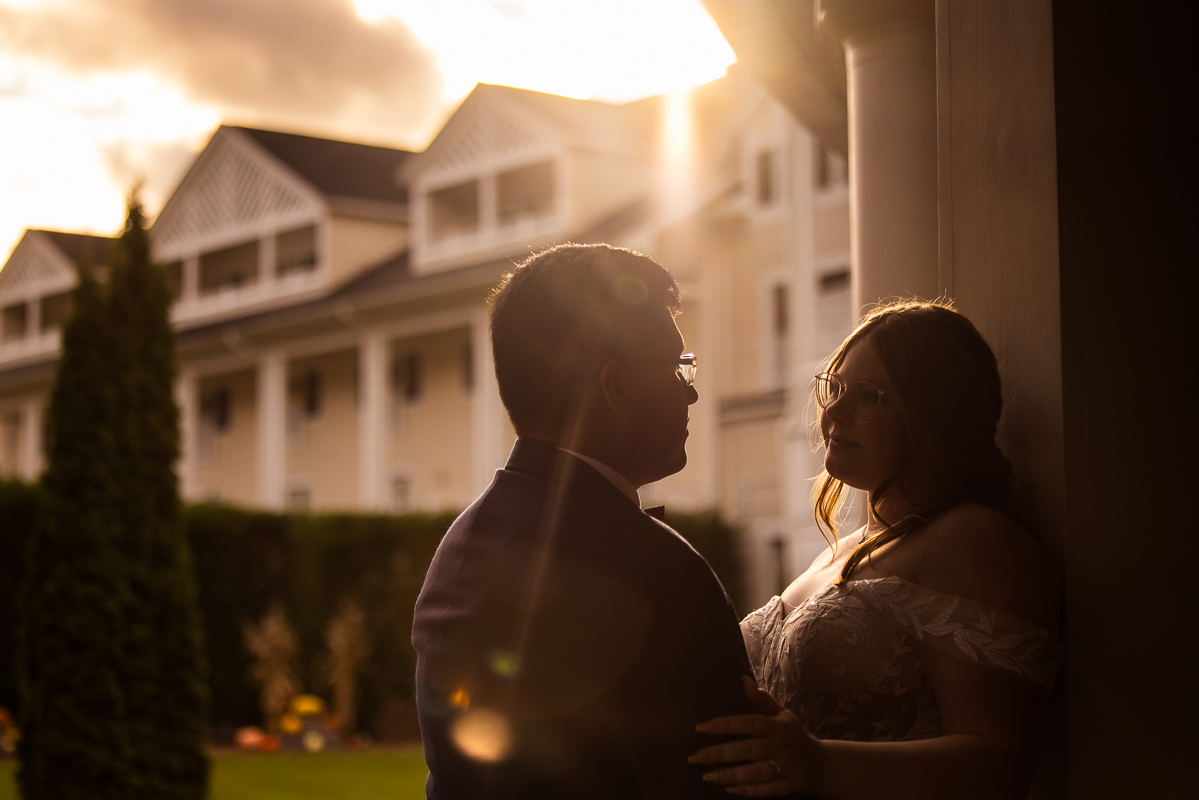 creative Omni wedding photographer, lisa rhinehart, captures this golden hour romantic portrait of the bride and groom as they look into one another's eyes with the sun beaming down on them as the omni bedford springs resort is behind them in these sunset portraits