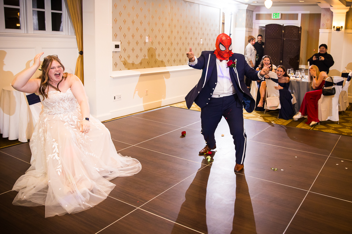 creative Omni wedding photographer, lisa rhinehart, captures this fun, unique image of the groom as he shows off his spiderman mask and poses like spiderman while the bride laughs during this unique, fun wedding reception at the omni bedford springs resort in pa 
