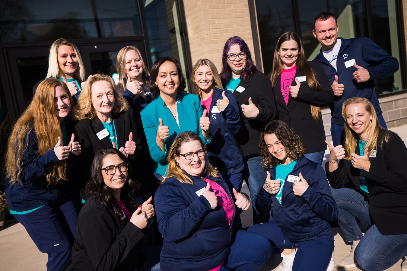 lisa rhinehart, pa branding photographer, captures this image of the orthodontic staff as they huddle together outside of their newly renovated building as put their thumbs up at the camera 