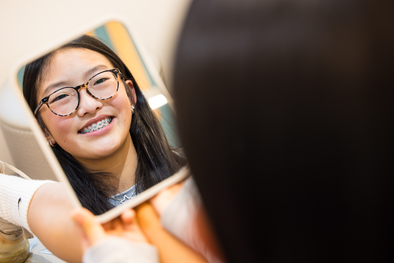 pa branding photographer, lisa rhinehart, captures this creative unique portrait of this patient looking at herself in the mirror smiling while looking at her braces during her orthodontist appointment at west chester orthodontics 