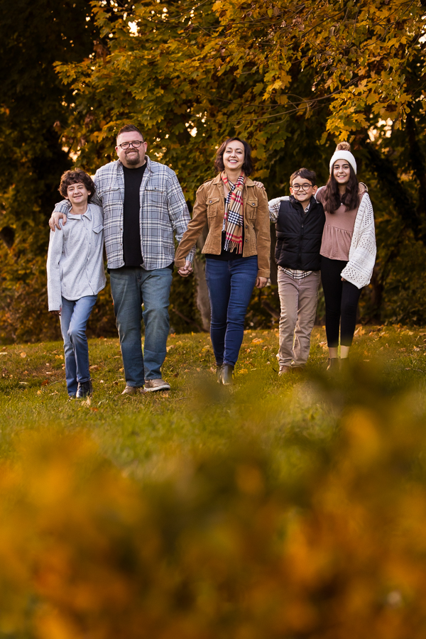 pa family photographer, lisa rhinehart, captures this traditional shot of this family as they walk together with the vibrant, colorful fall leaves falling around them 