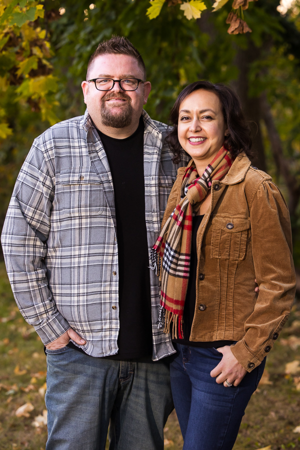 west chester portrait photographer, lisa rhinehart, captures this image of husband and wife as they stand beside one another and smile at the camera during this outdoor portrait session surrounded by vibrant, colorful fall leaves 