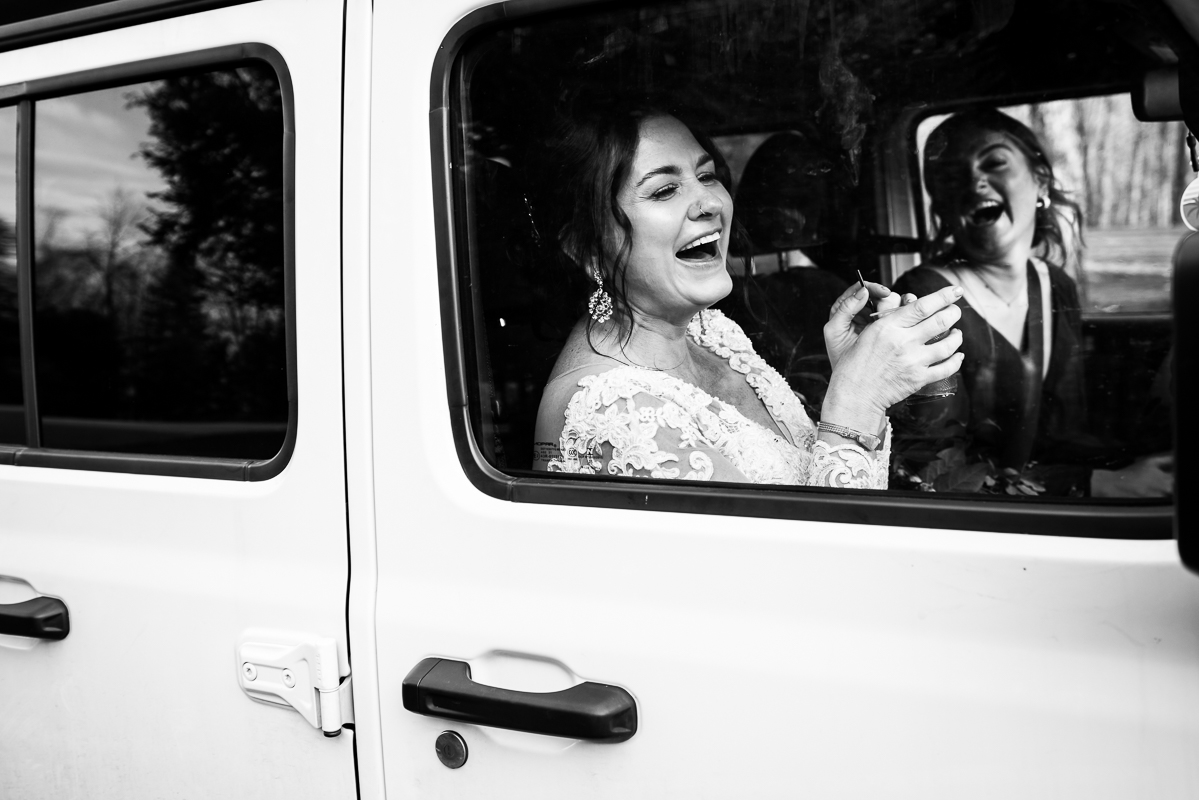 candid wedding photographer, lisa rhinehart, captures this authentic moment between the bride and her bridesmaid inside of this white jeep as they get ready to drive off before this Christmas winter wedding ceremony in stroudsmoor pa 