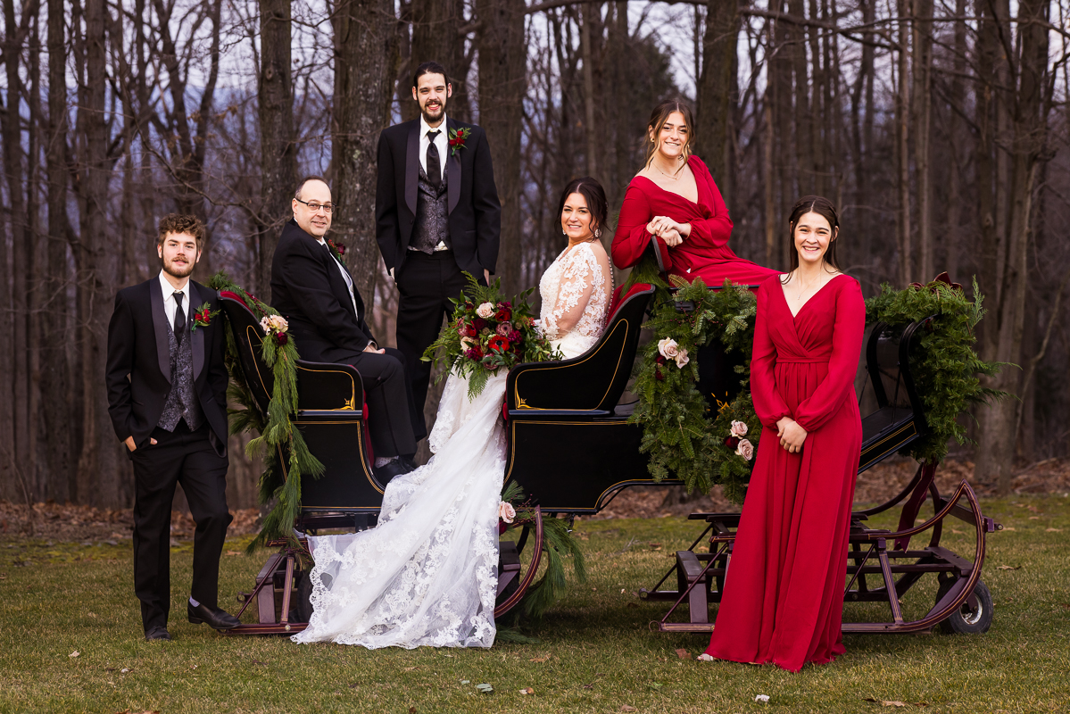 stroudsmoor winter wedding photographer, Lisa rhinehart, captures this image of the bride and groom with their wedding party as they pose on and around this sleigh before their outdoor christmas wedding 