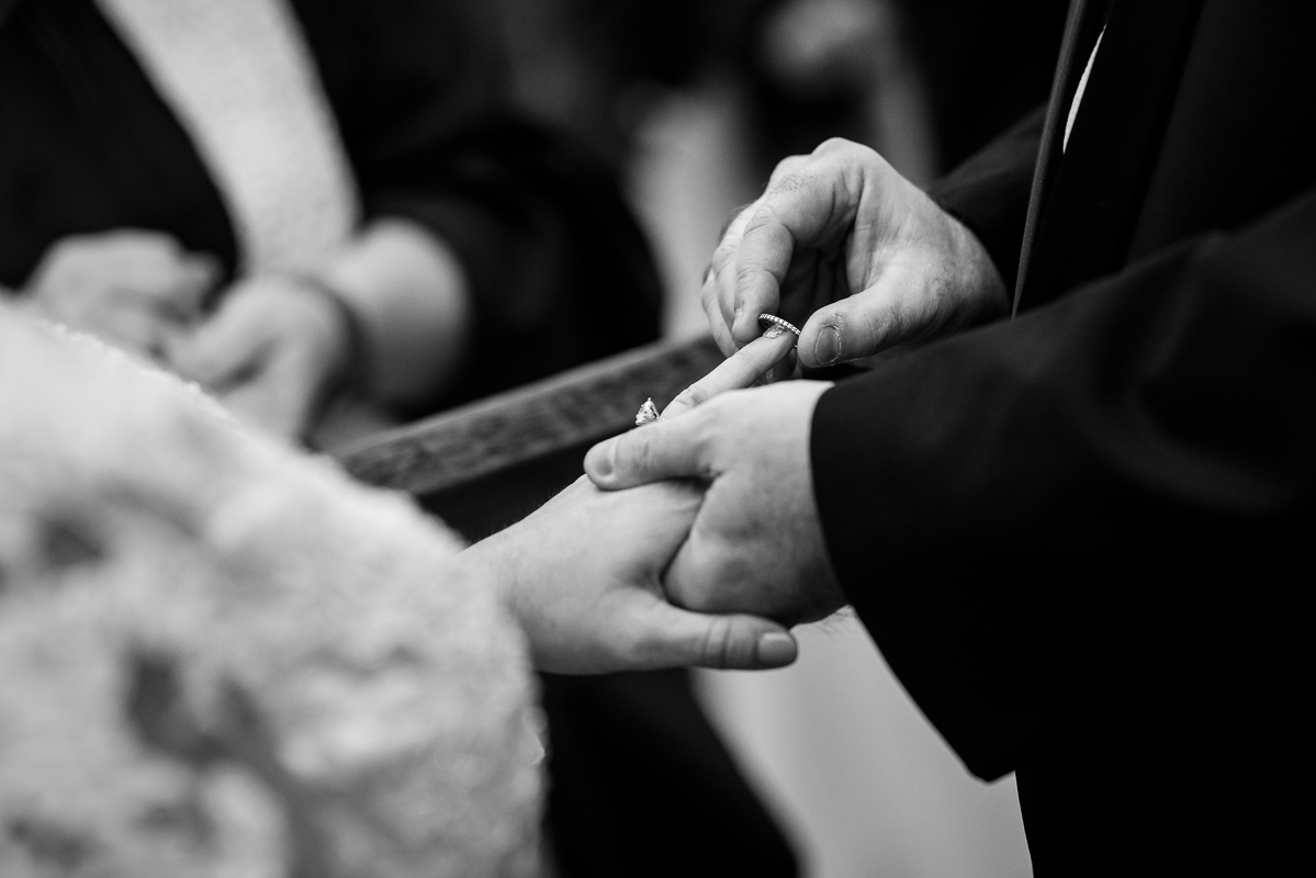 detail wedding photographer, lisa rhinehart, captures this close up black and white image of the bride and groom as they exchange wedding rings during this outdoor winter wedding ceremony 
