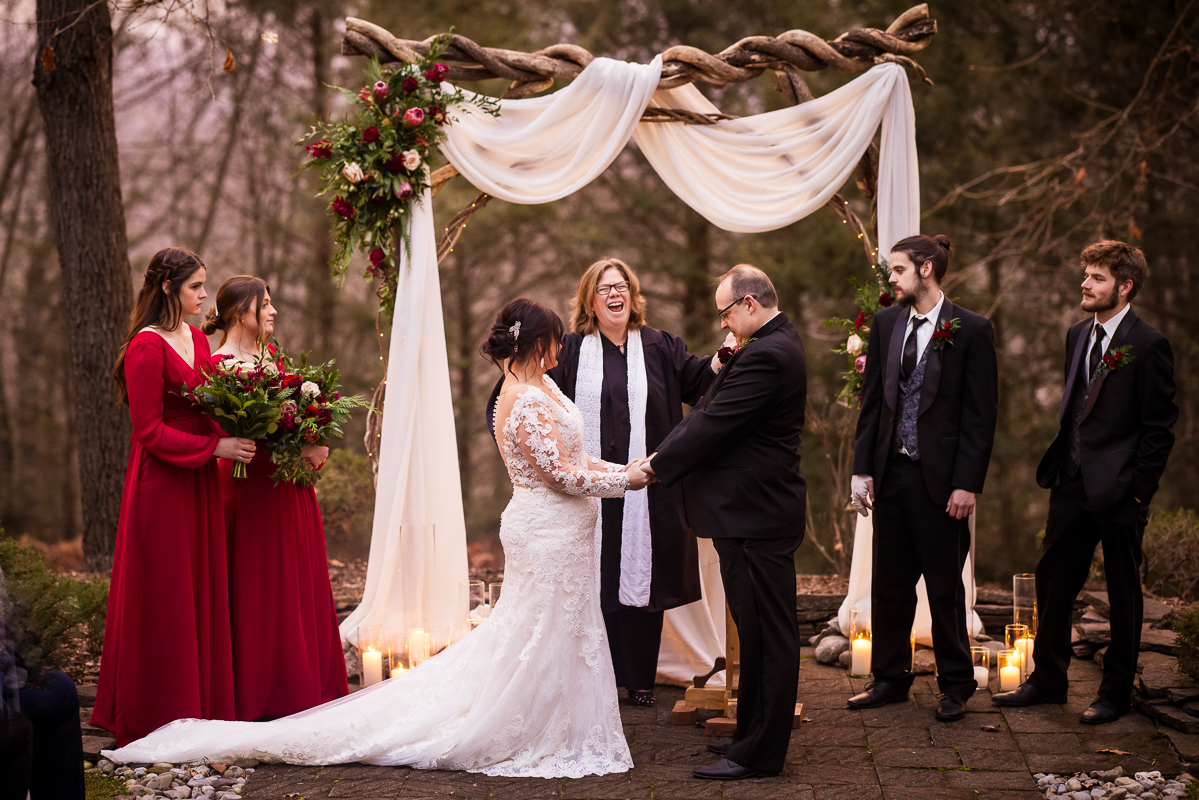stroudsmoor winter wedding photographer, lisa rhinehart, captures this outdoor Christmas wedding ceremony of the bride and groom holding hands before they share their first kiss at the auradell in the stroudsmoor country inn