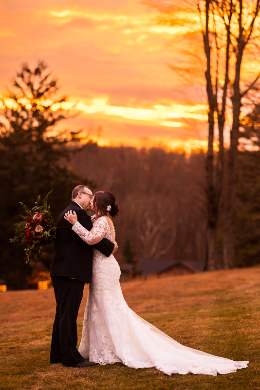 best pa wedding photographer, lisa rhinehart, captures this vibrant, colorful image of the bride and groom as they share a kiss while the vibrant sun sets behind them during their outdoor stroudsmoor winter wedding 