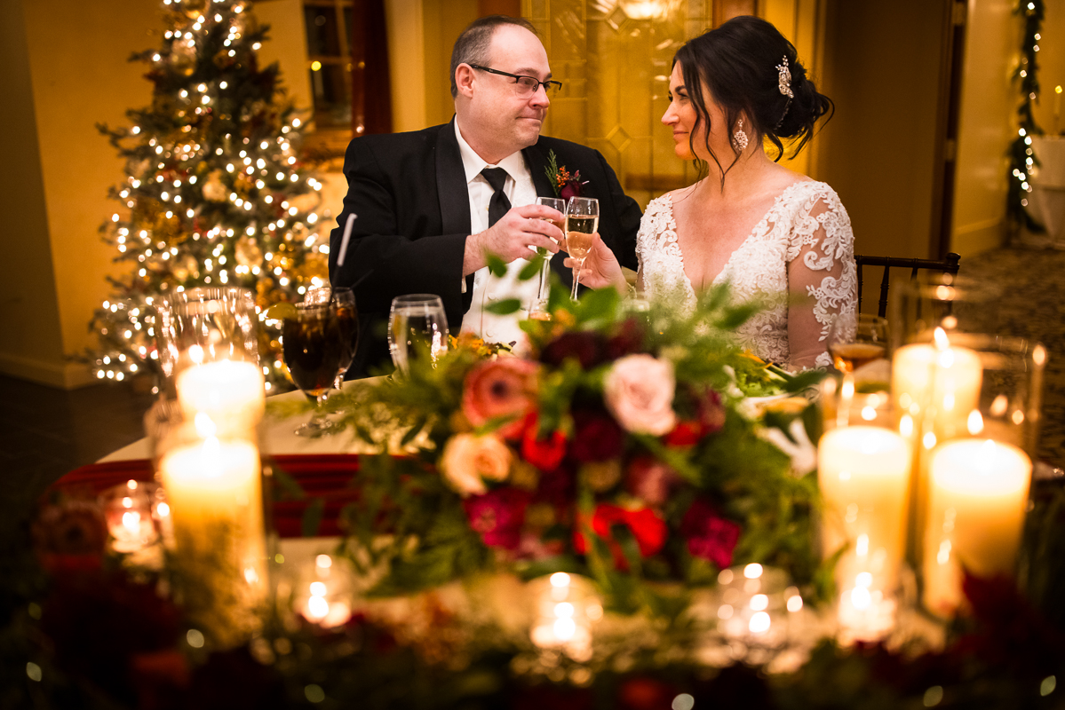 stroudsmoor winter wedding photographer, Lisa rhinehart, captures this image of the bride and groom as they share a toast together while surrounded by the cozy warm Christmas lights, Christmas tree and candles during this classic, timeless winter wedding reception at the stroudsmoor country inn 