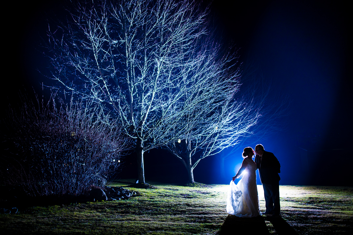 Stroudsmoor Winter Wedding photographer, lisa rhinehart, captures this end of the night shot of the bride and groom as they share a kiss together outside underneath the bare winter trees in pa