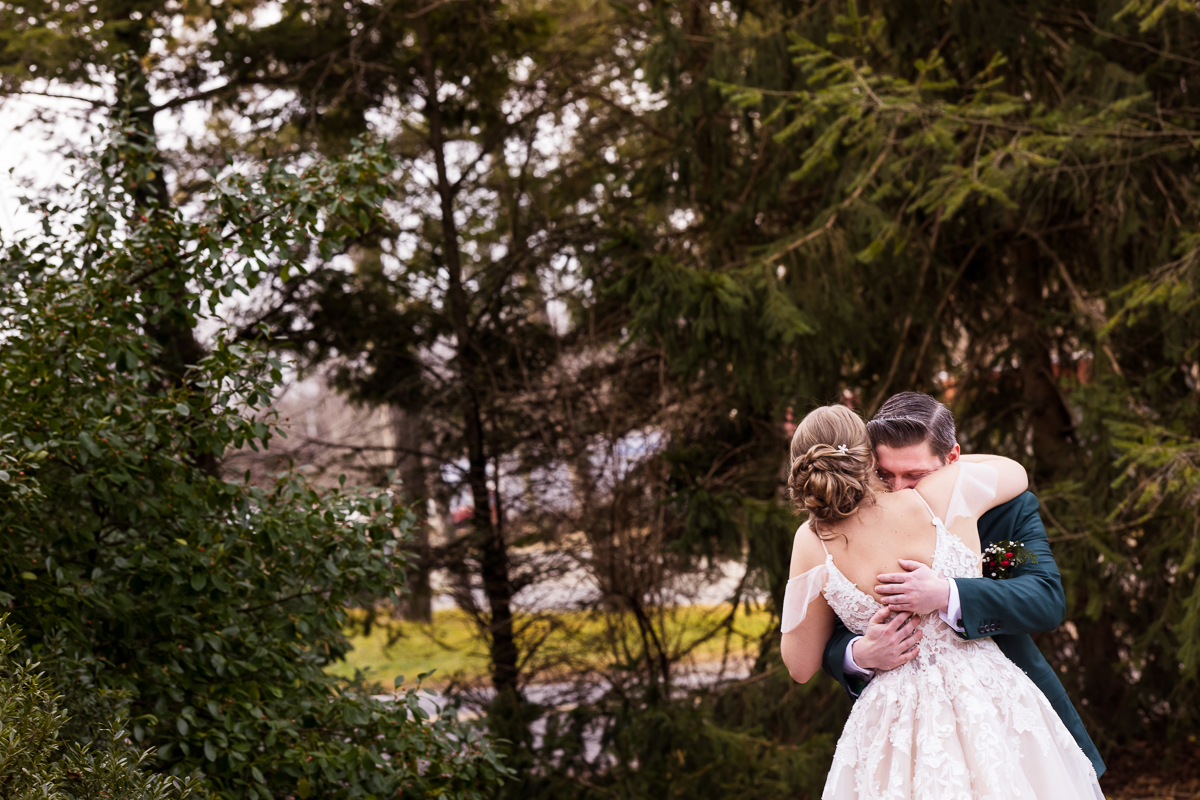 image of the bride and groom as they share a hug during their outdoor Christmas first look before their Christmas stone mill inn wedding 