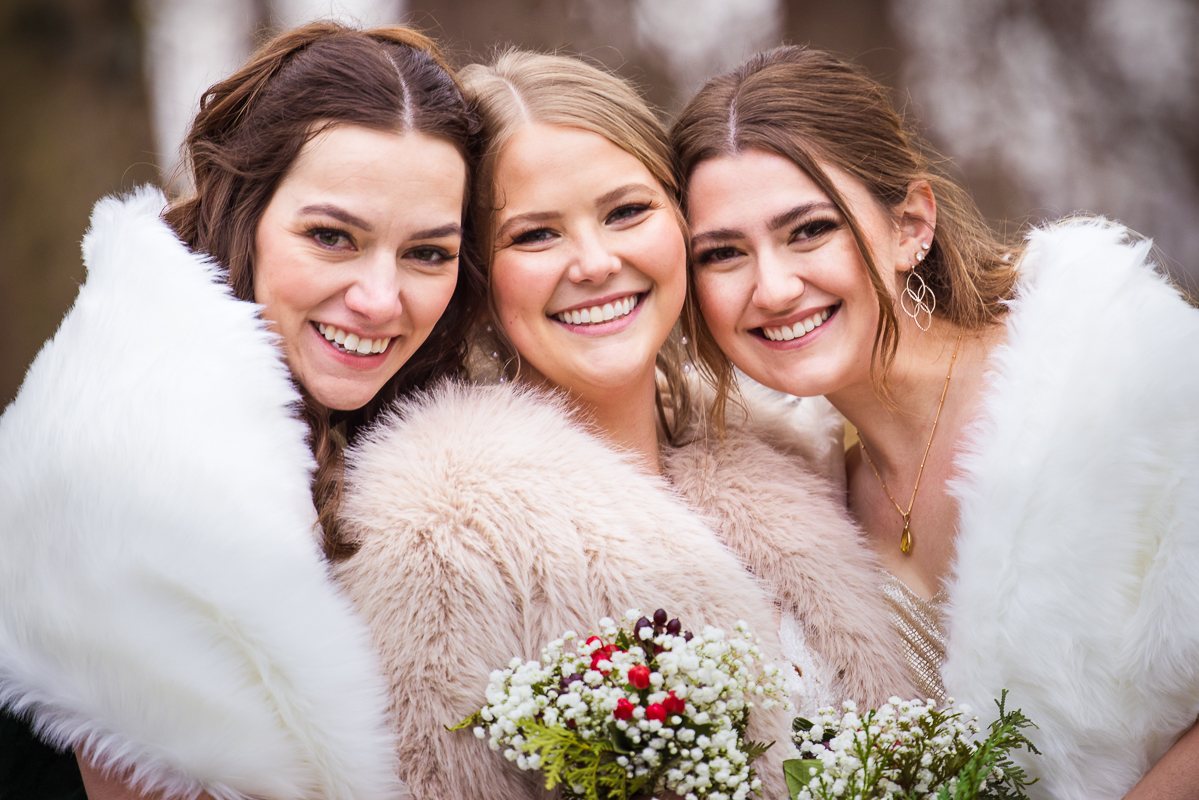close up traditional portrait of the bride with two of her bridesmaids hugging one another during before this outdoor Christmas wedding 