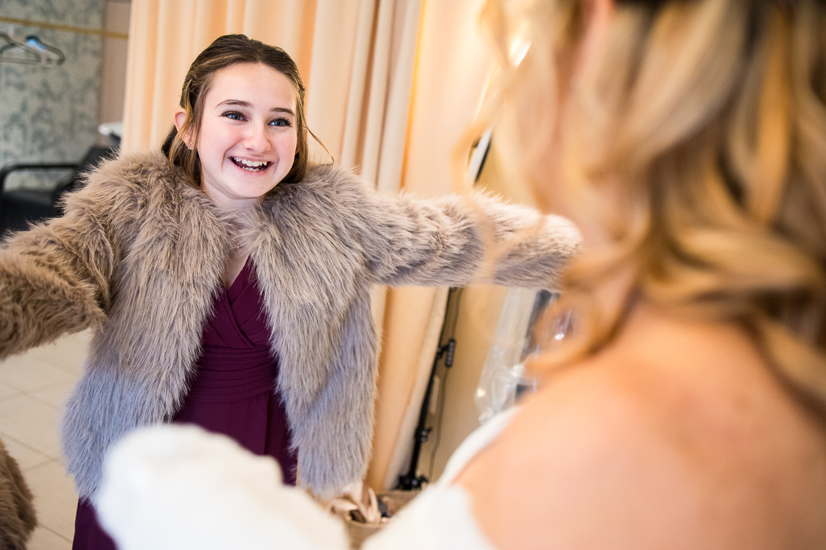 unique perspective of the daughter of the bride showing off her dress and fur jacket after finishing her hair and makeup in the salt spa at the reeds of shelter haven