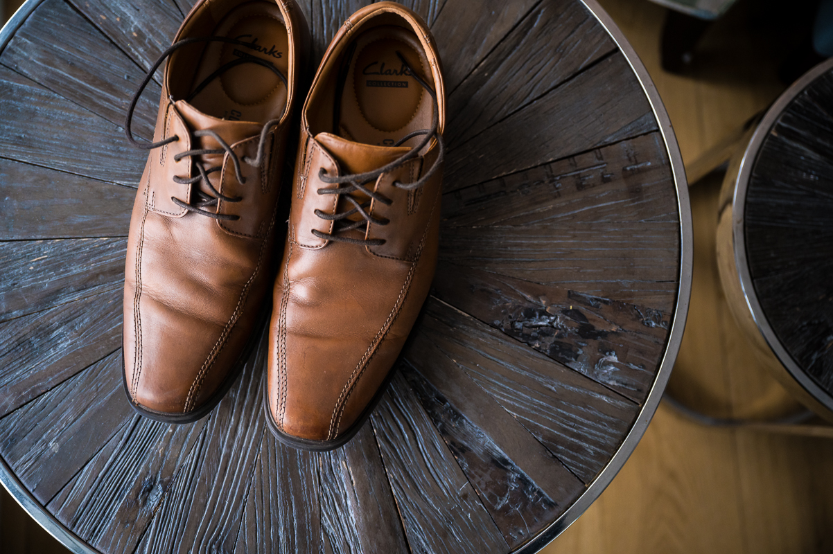 image of the grooms brown shoes as they sit on a unique wooden table during the wedding preparations before this outdoor Christmas wedding at the reeds on the beach 