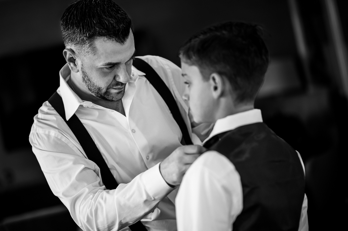 candid wedding photographer, rhinehart photography, captures this black and white image of the groom as he fixes his sons outfit before finishing morning wedding preparations at the reeds in New Jersey