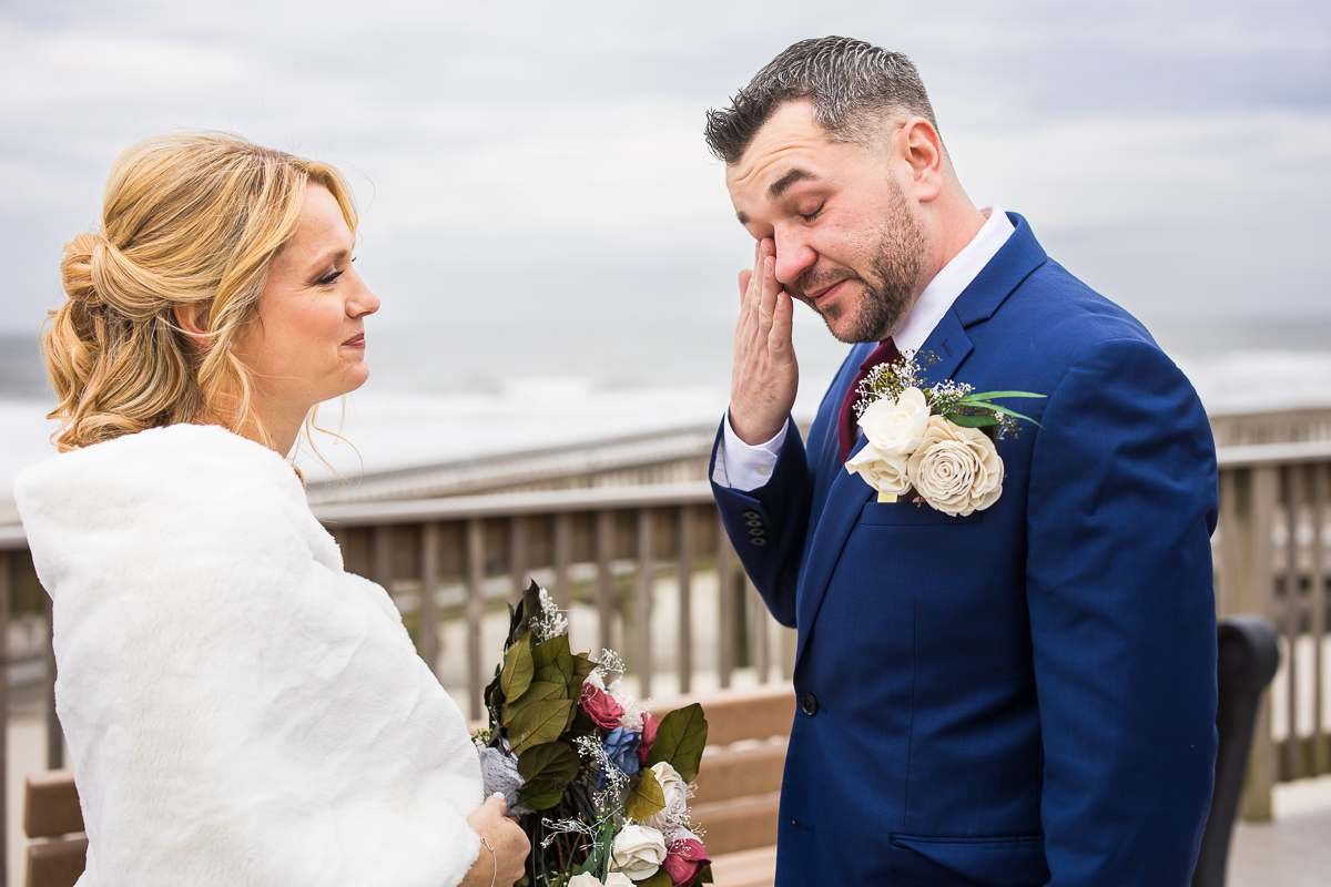 image of the bride and groom as they smile at one another and wipe tears away during this emotional first look located on the beach during this Winter Reeds Stone Harbor Wedding
