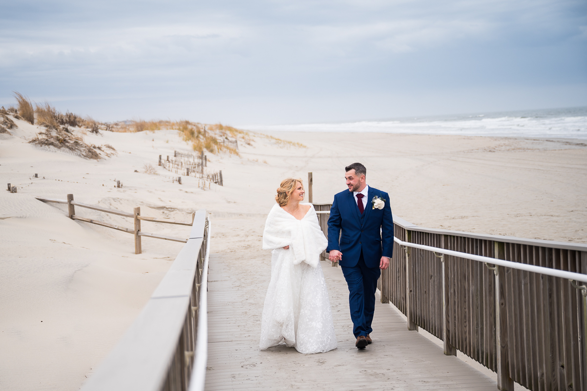 image of the bride and groom as they walk up the ramp from the beach holding hands together before this Winter Reeds Stone Harbor Wedding ceremony located by the beach in New Jersey 