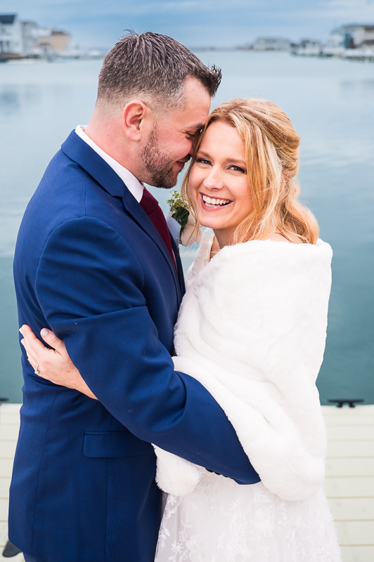 fun, loving image of the bride and groom as they hug one another beside the vibrant blue water during this romantic beach first look before this winter wedding ceremony in New Jersey 