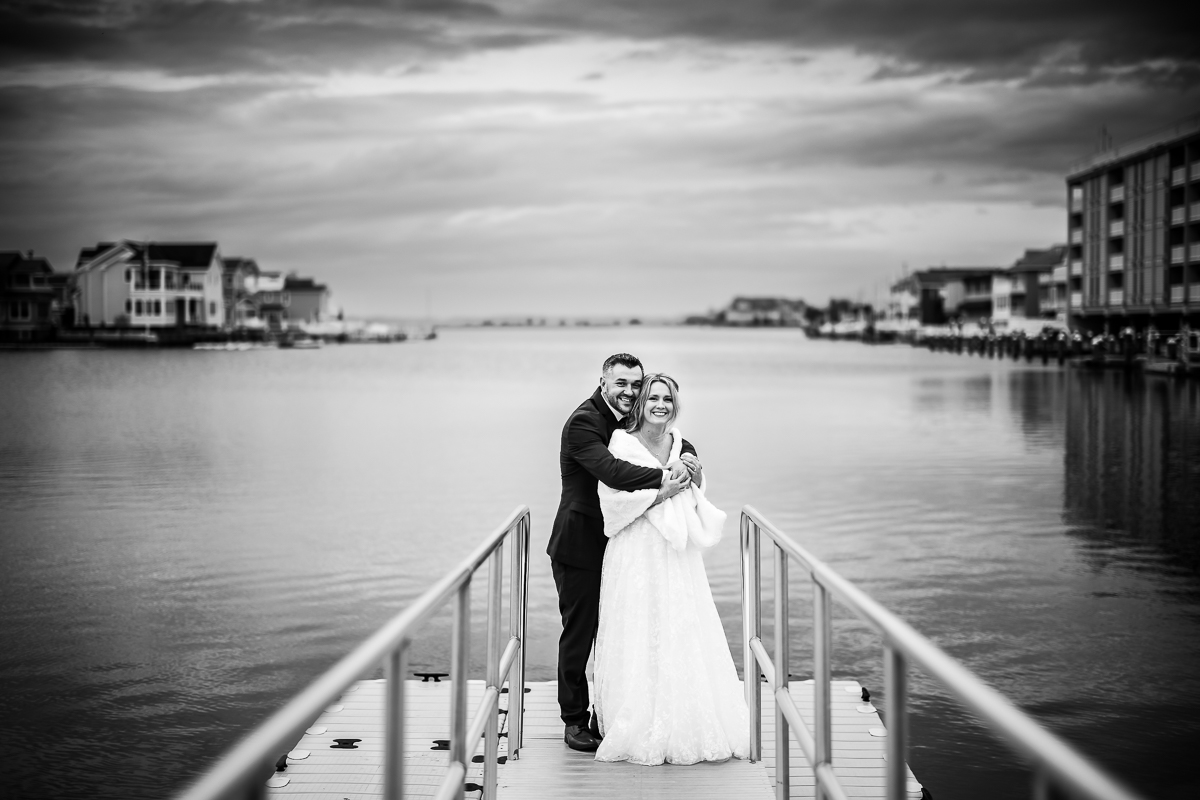 best nj wedding photographer, rhinehart photography, captures this stunning black and white image of the bride and groom as they hug one another on the dock during their outdoor beach first look at this Winter Reeds Stone Harbor Wedding