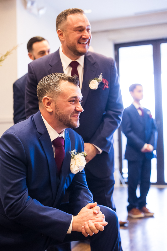emotional, sentimental image of the groom and his best man as they watch as people walk down the aisle during their indoor Christmas wedding ceremony in New Jersey at the reeds