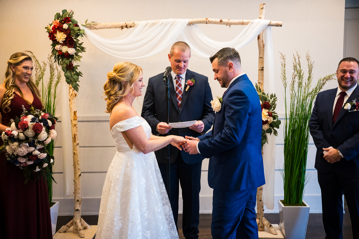 traditional image of the bride and groom as they stand together holding hands at the alter during this indoor winter beach wedding captured by the reeds wedding photographer, rhinehart photography