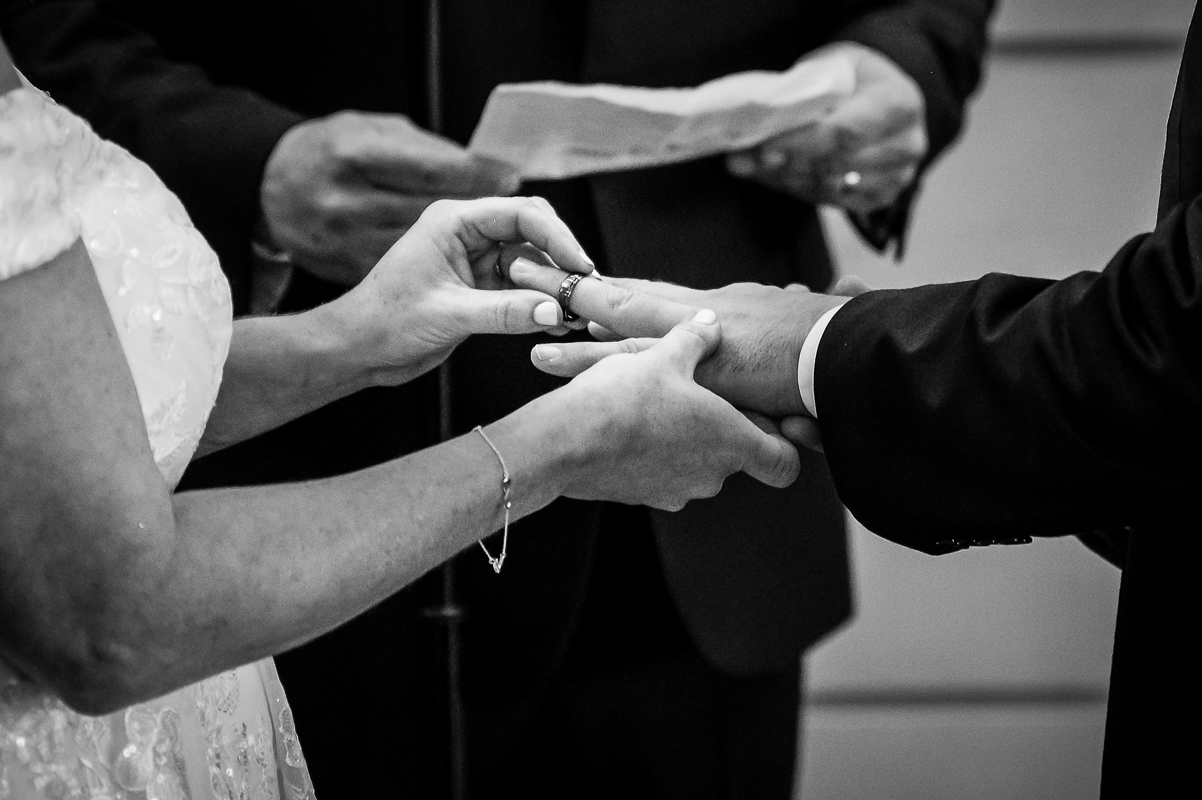 black and white close up detail image of the bride and groom as they place rings on their fingers during this emotional winter wedding ceremony at the reeds in New Jersey 