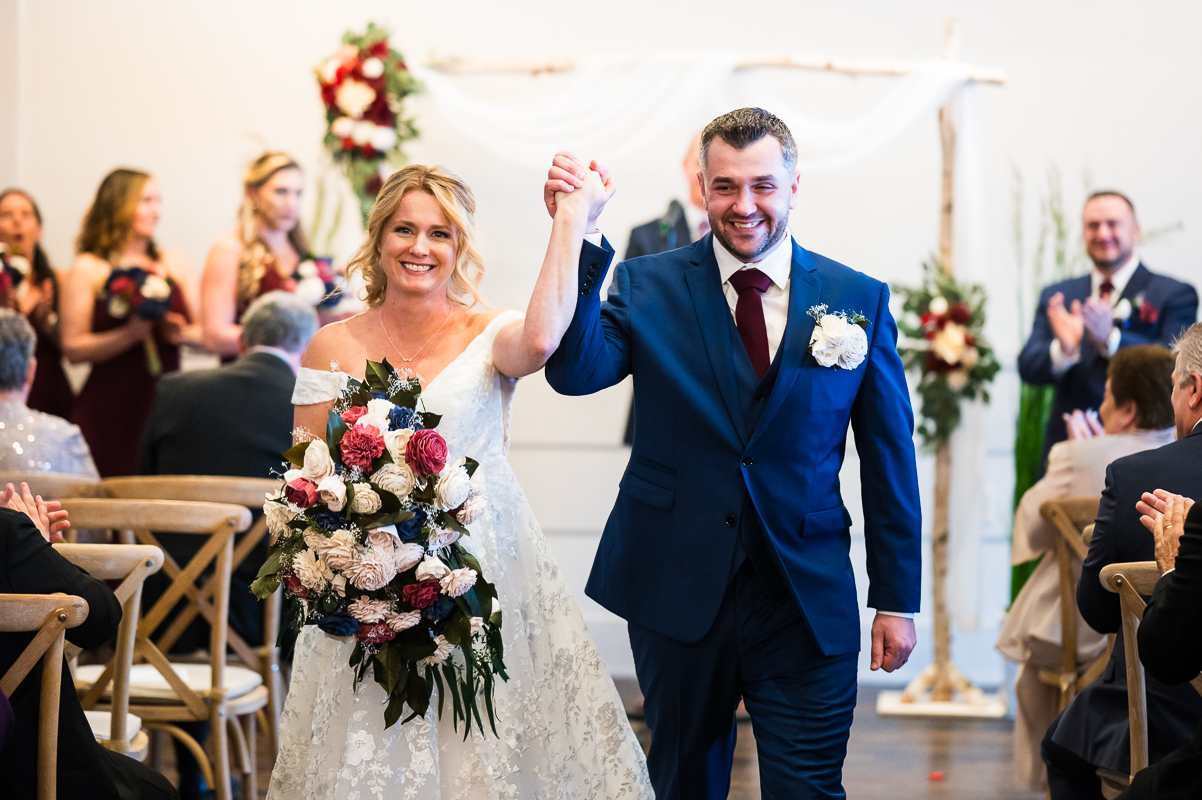image of the bride and groom as they walk down the aisle after their Christmas wedding ceremony cheering that they are officially married at this indoor beach wedding ceremony 
