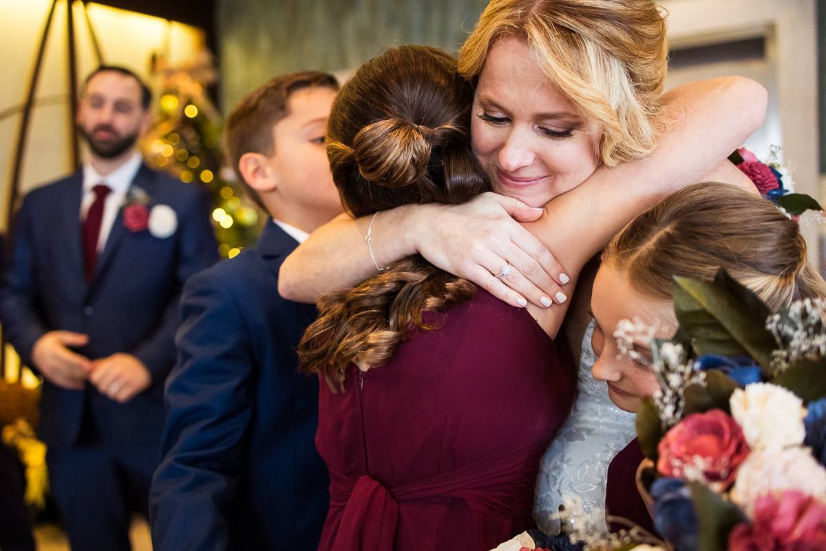sentimental image of the bride as she hugs her children after this winter wedding ceremony at the reeds at shelter haven by the beach in New Jersey 