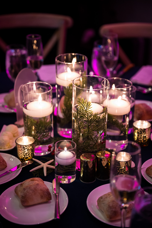 detail image of the centerpieces on each table during this Christmas beach wedding reception featuring candles, pine, and starfish