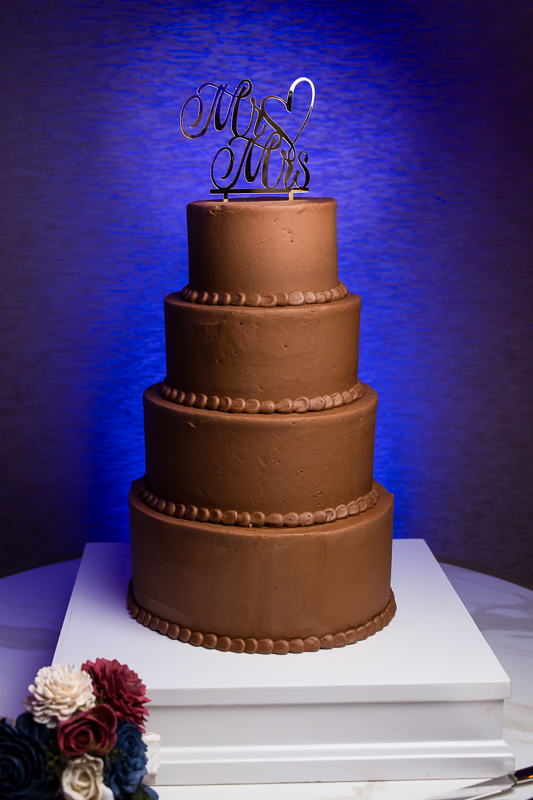 detail wedding photographer, rhinehart photography, captures this vibrant image of the chocolate four tiered wedding cake against this vibrant blue wall before this Christmas wedding reception 