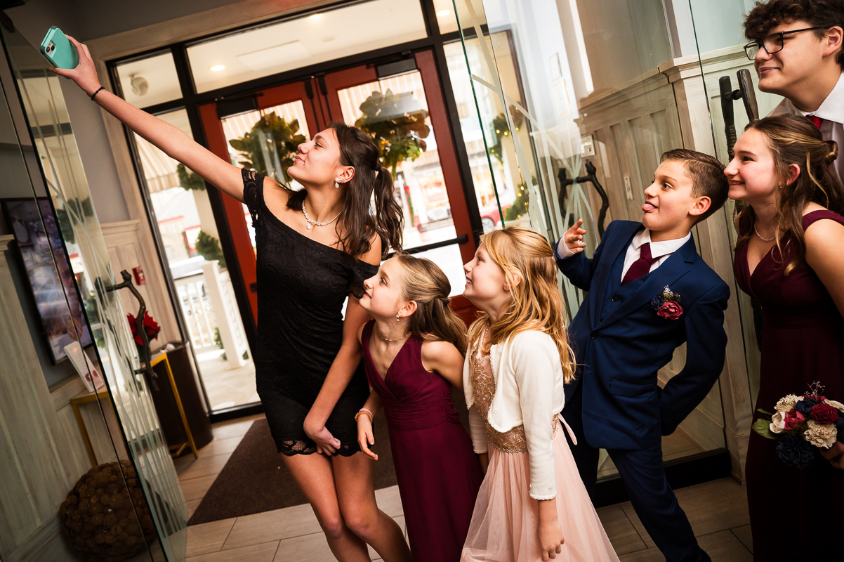fun, candid moment captured by family wedding photographer, rhinehart photography, of the kids taking a selfie together during this fun, Christmas wedding reception at the reeds at shelter haven 