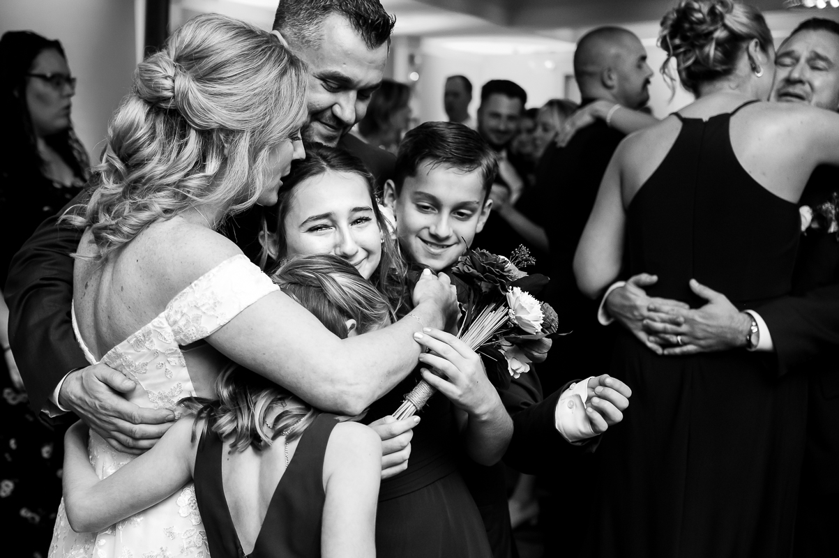 candid, emotional black and white image of the bride, groom and their children as they all dance together at this winter stone harbor wedding reception in New Jersey by the beach 