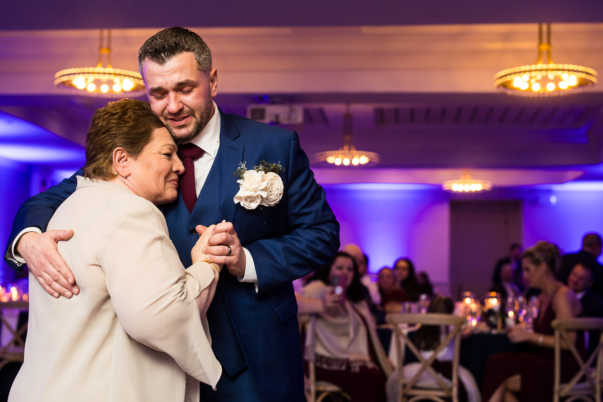 vibrant, colorful image of the groom and his mom as they share an emotional mother son dance together during this seaside winter wedding reception at the reeds at stone harbor in New Jersey 