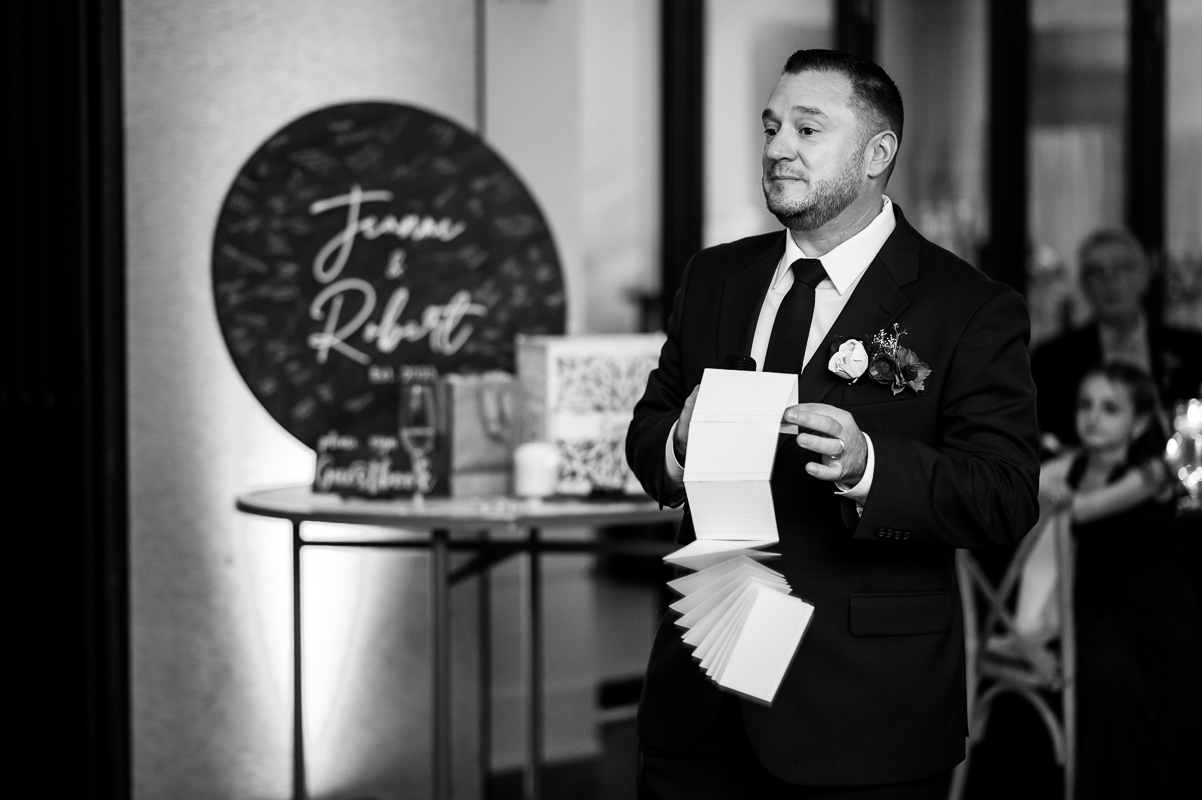black and white image of the best man as he shows how long his speech is during the traditions portion during this wedding reception at the reeds at shelter haven in New Jersey 