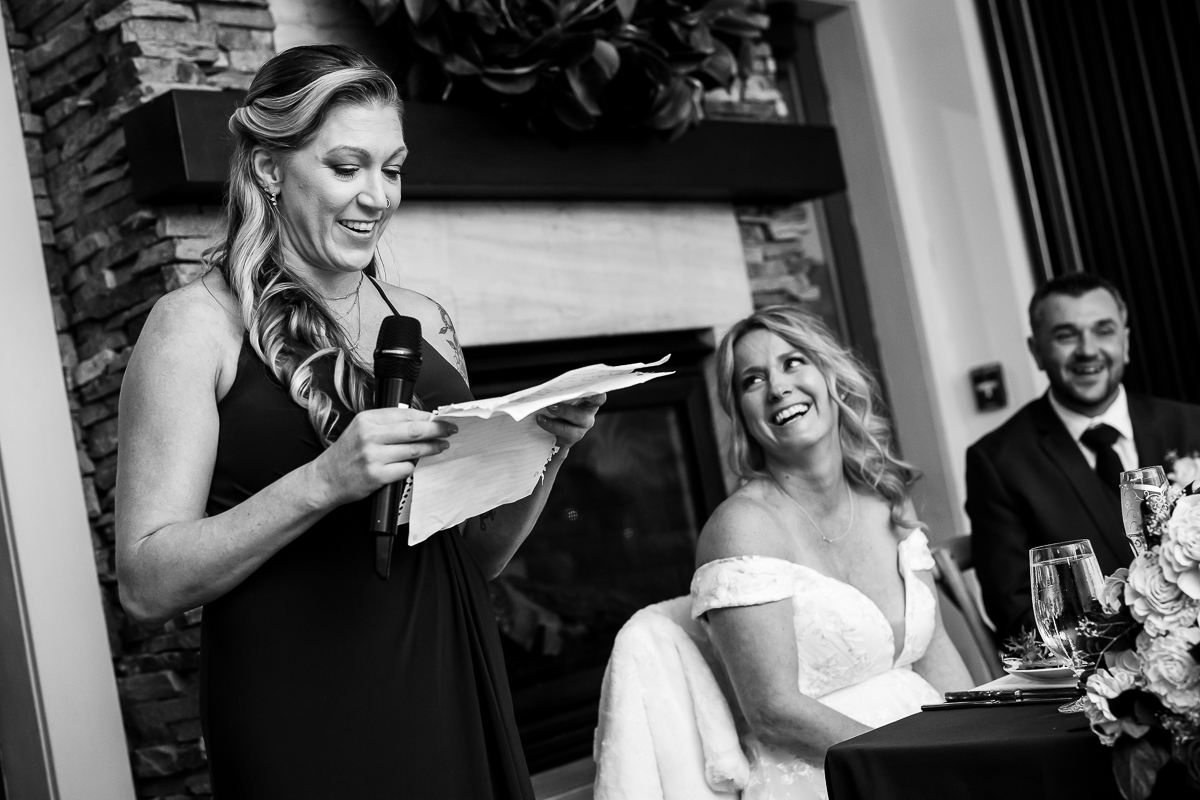 candid wedding photographer, rhinehart photography, captures this black and white image of the maid of honor as she shares her speech while everyone laughs during the wedding traditions portion of this winter wedding reception in New Jersey 