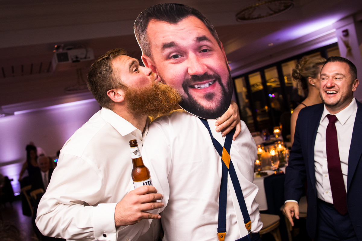fun image of a guest as he kisses the fat head of the groom during this fun winter wedding reception at the reeds in New Jersey 