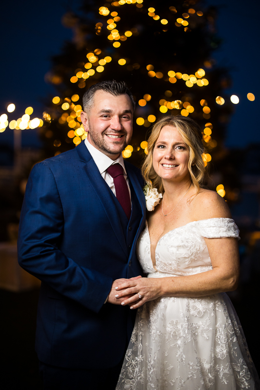 Winter Reeds Stone Harbor Wedding photographer, captures this traditional romantic portrait of the bride and groom as they stand together infront of this giant Christmas tree during this winter wedding 