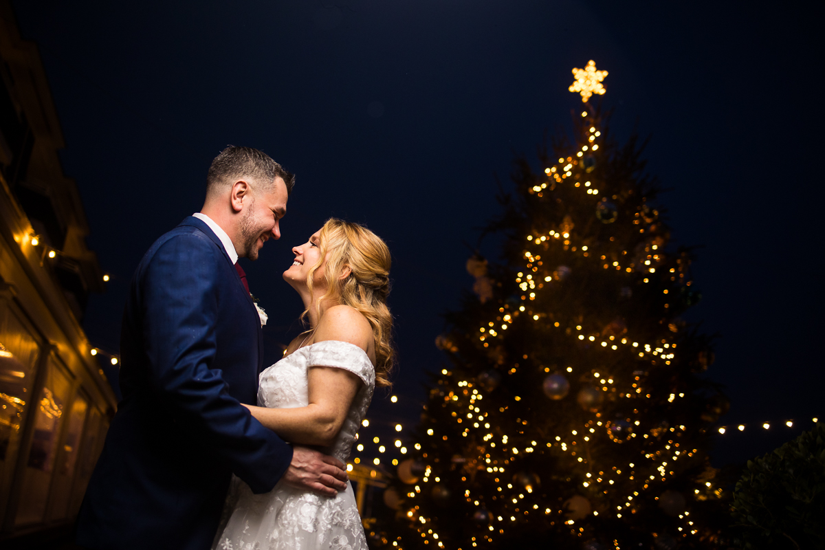 romantic end of the night portrait of the bride and groom as they stand together in front of the giant Christmas tree by the beach for this Winter Reeds Stone Harbor Wedding in New Jersey 